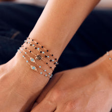 Photo de la main d’une femme portant différents bracelets Gigi Clozeau aux couleurs turquoise et noires.