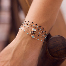 Photo de la main d’une femme portant différents bracelets Gigi Clozeau aux couleurs turquoise et noires.