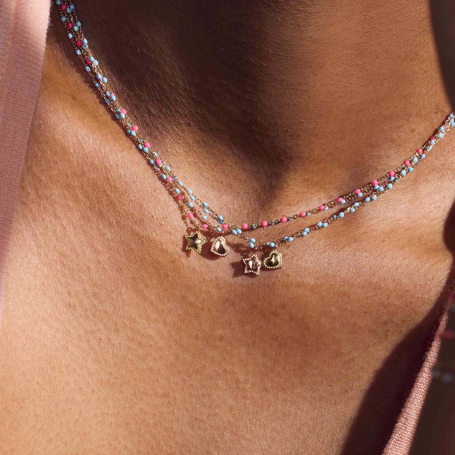 Photo du décolleté d’une femme portant des colliers Gigi Clozeau de la collection Capsule Summer en rose fluo et turquoise.