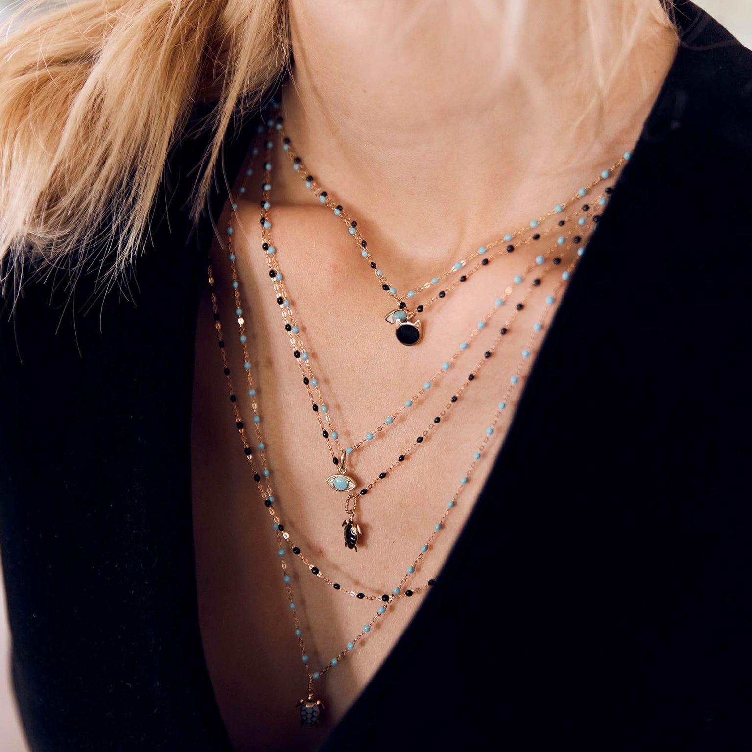 Photo du cou d’une femme portant différents colliers Gigi Clozeau aux couleurs turquoise et noires.