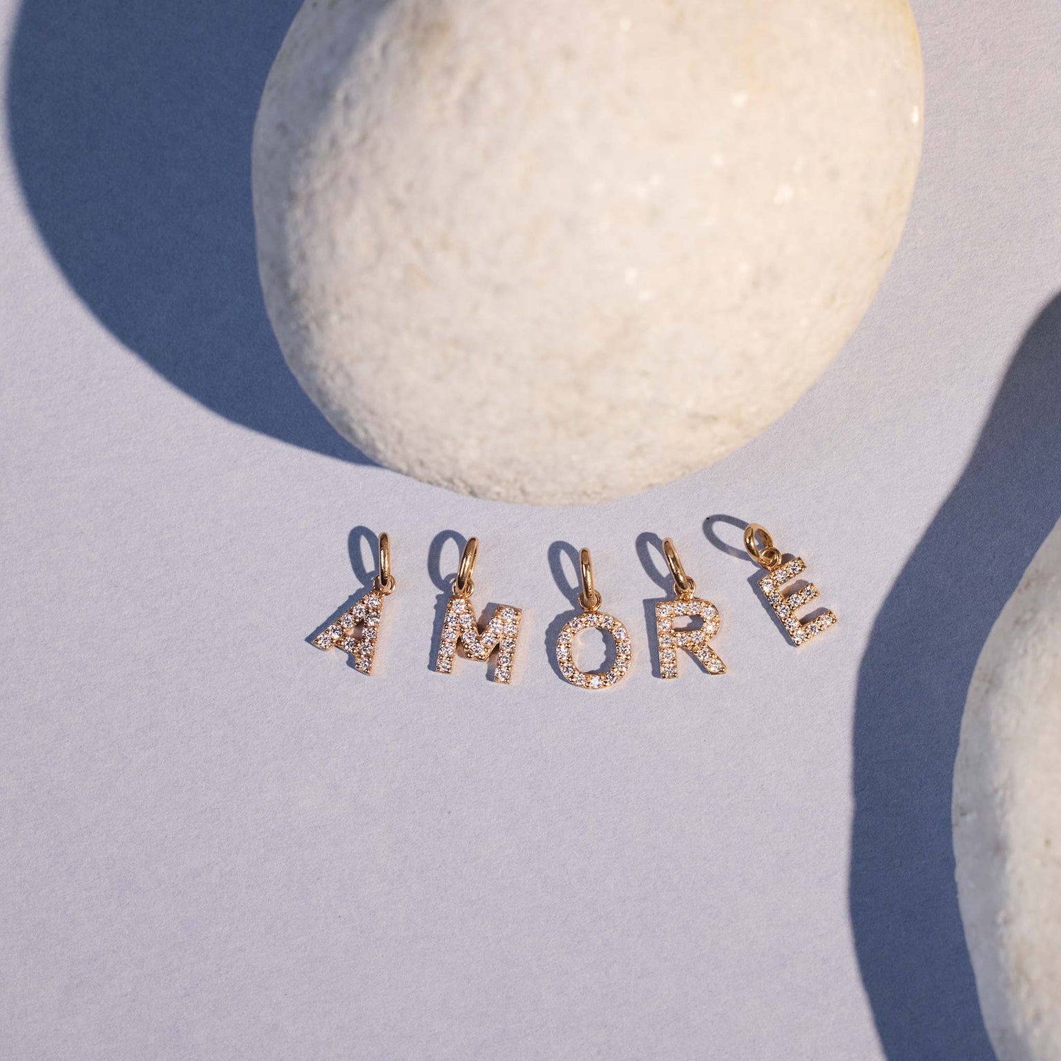 Photo de nature morte de plusieurs pendentifs Lucky Letters Gigi Clozeau posés, formant le mot « Amore ».