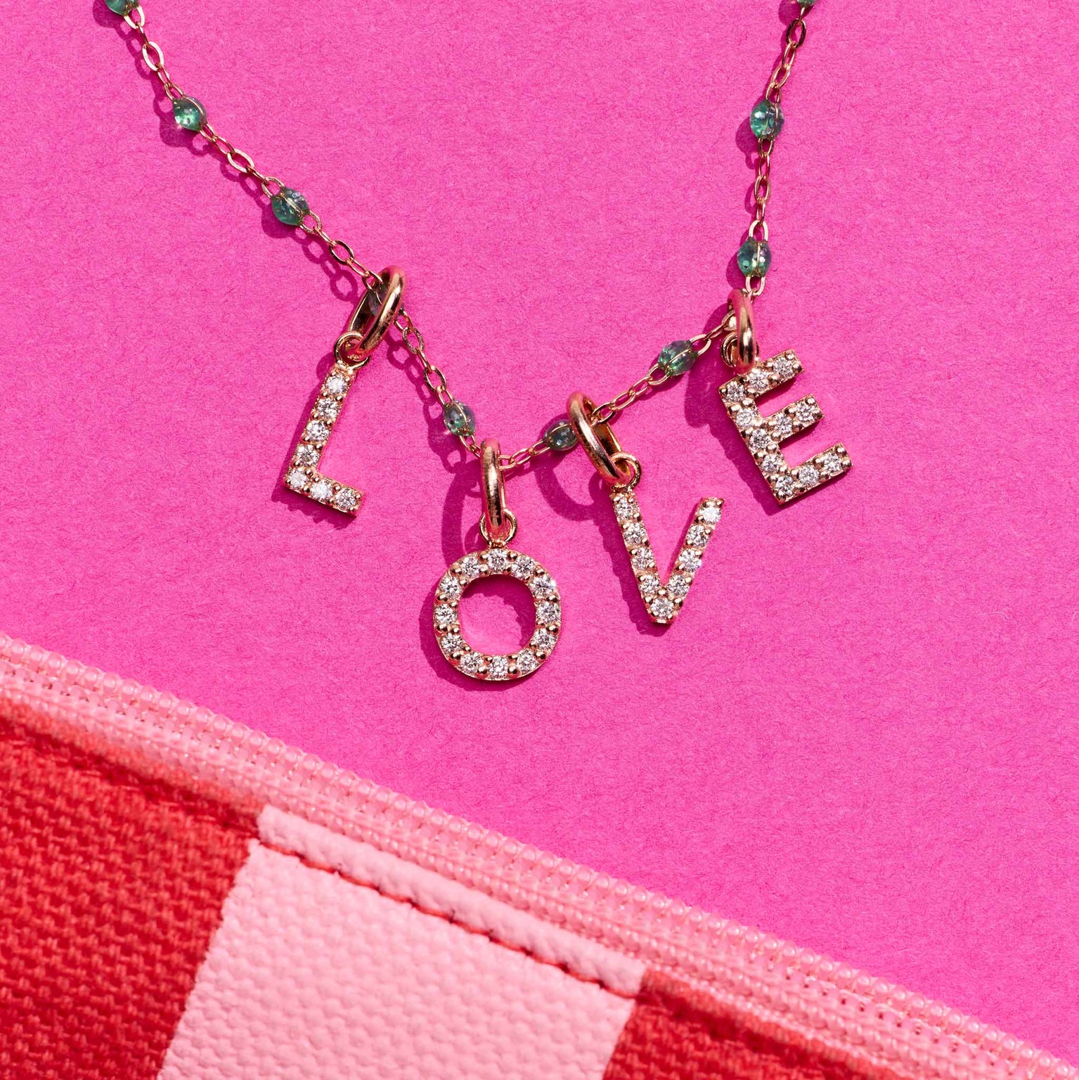 Photo des pendentifs Lucky Letters Gigi Clozeau posé sur un fond rose 